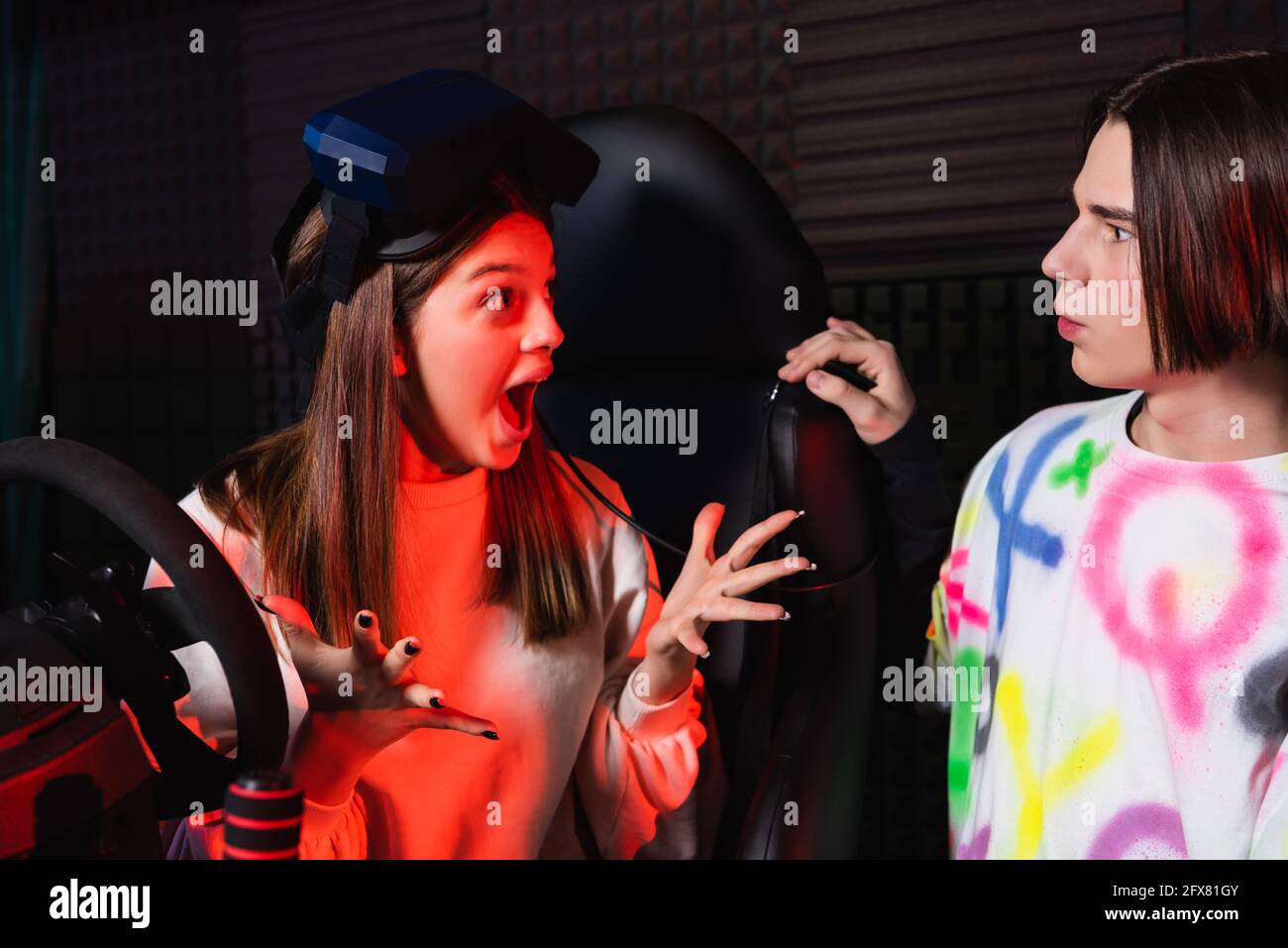 astonished girl gesturing while talking to friend near car simulator Stock Photo