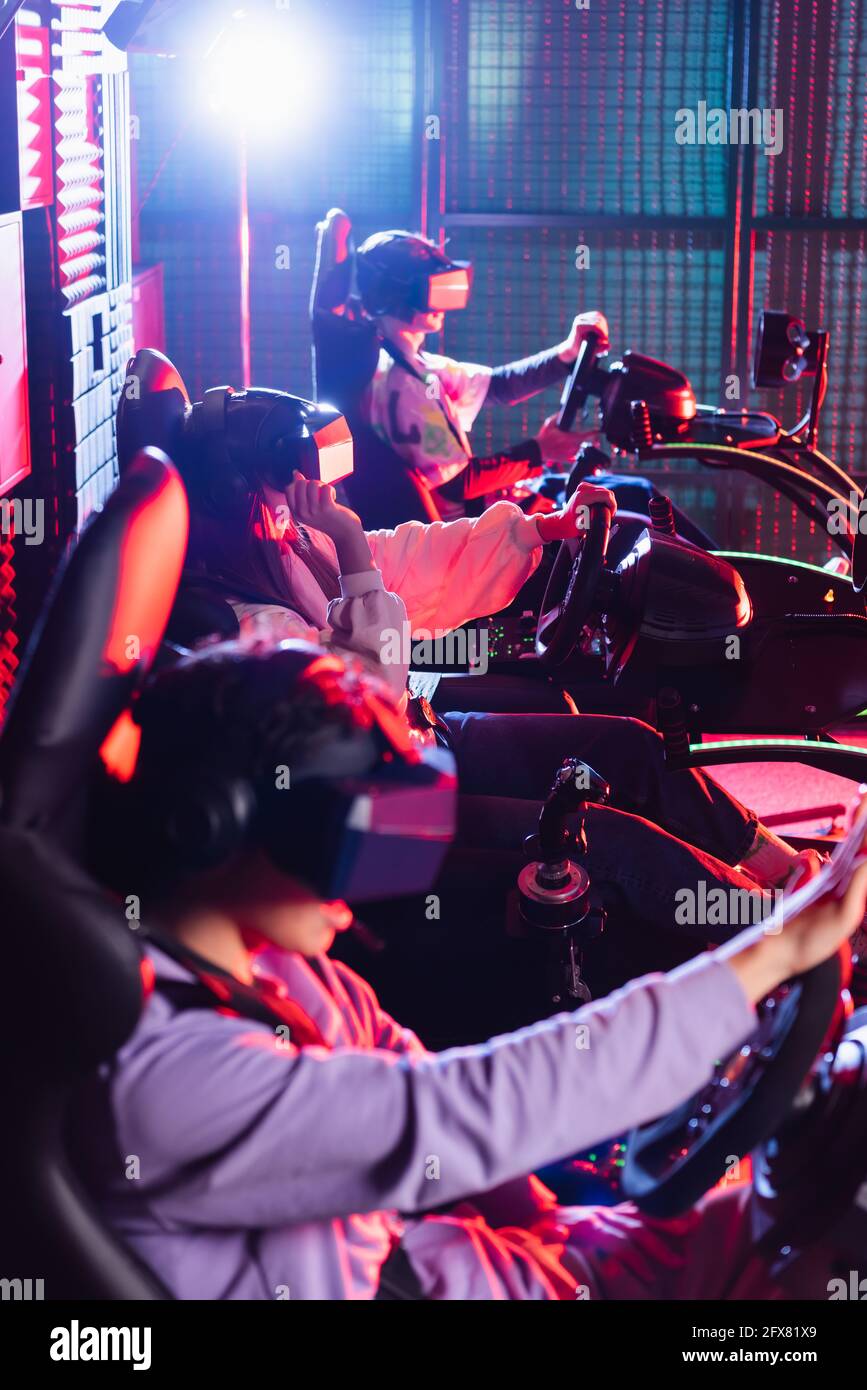 teenagers in vr headsets playing racing game in car simulators Stock