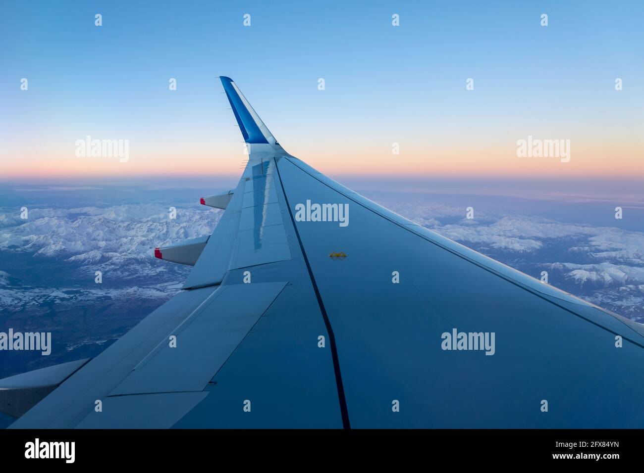 Airplane wing in flight over the Alps in winter at sunset, travel concept Stock Photo
