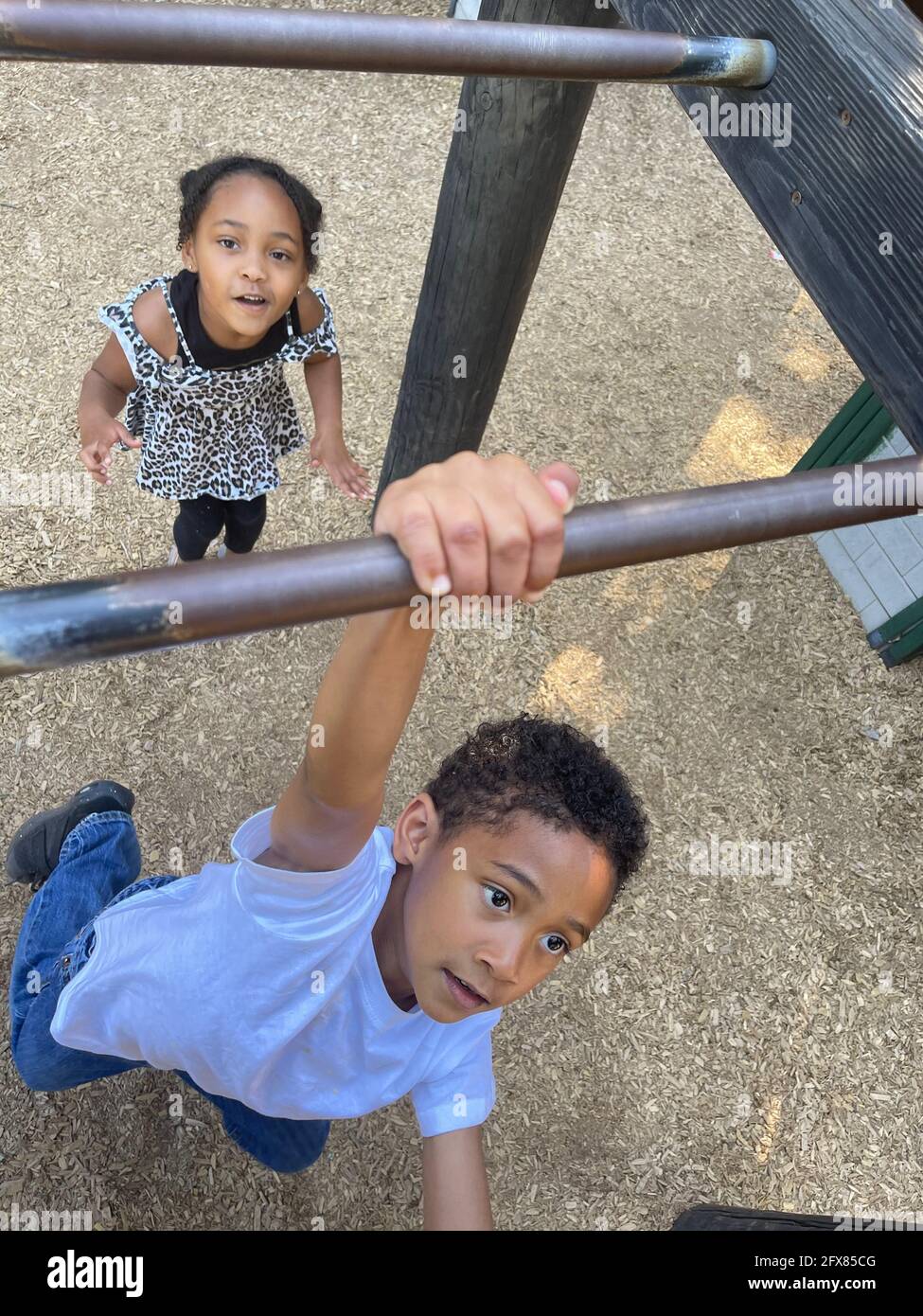Vertical shot of a black boy and girl playing in a park and swinging from monkey bars Stock Photo