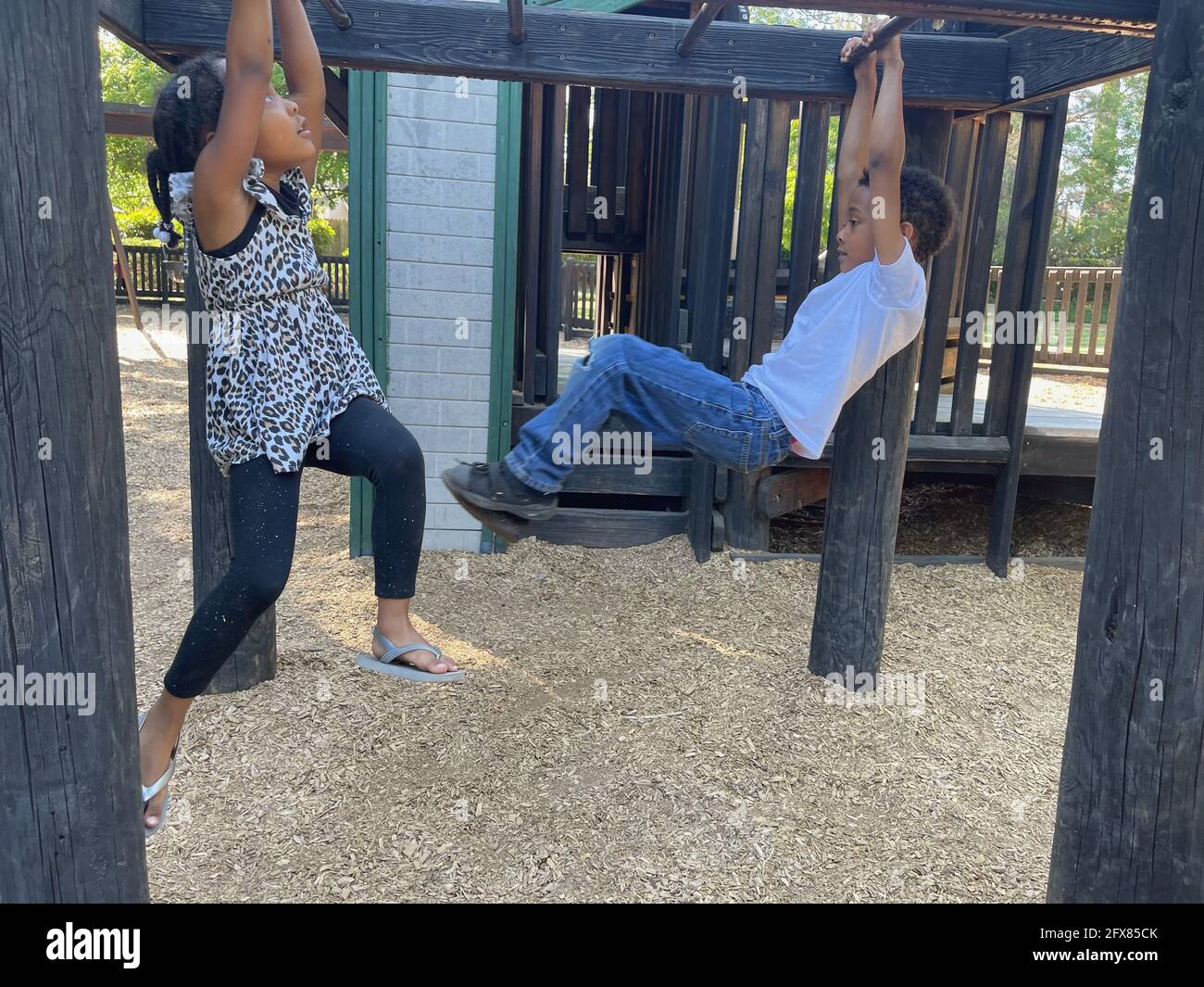 Pair of American children playing in a park and swinging from monkey bars Stock Photo