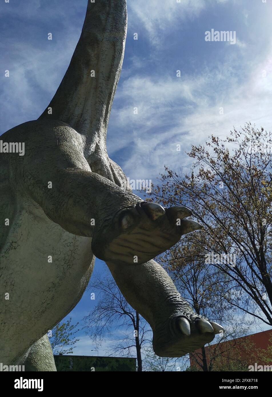 Vertical shot of a statue of a brachiosaurus dinosaur in a park with lifted front paws Stock Photo