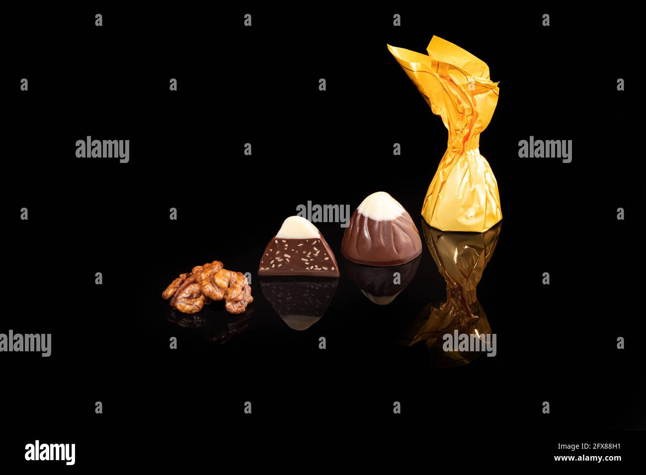 Chocolate candies on a dark background with reflection. Piece by piece and as a whole. Filling of nuts and fruits. Copy space. Stock Photo