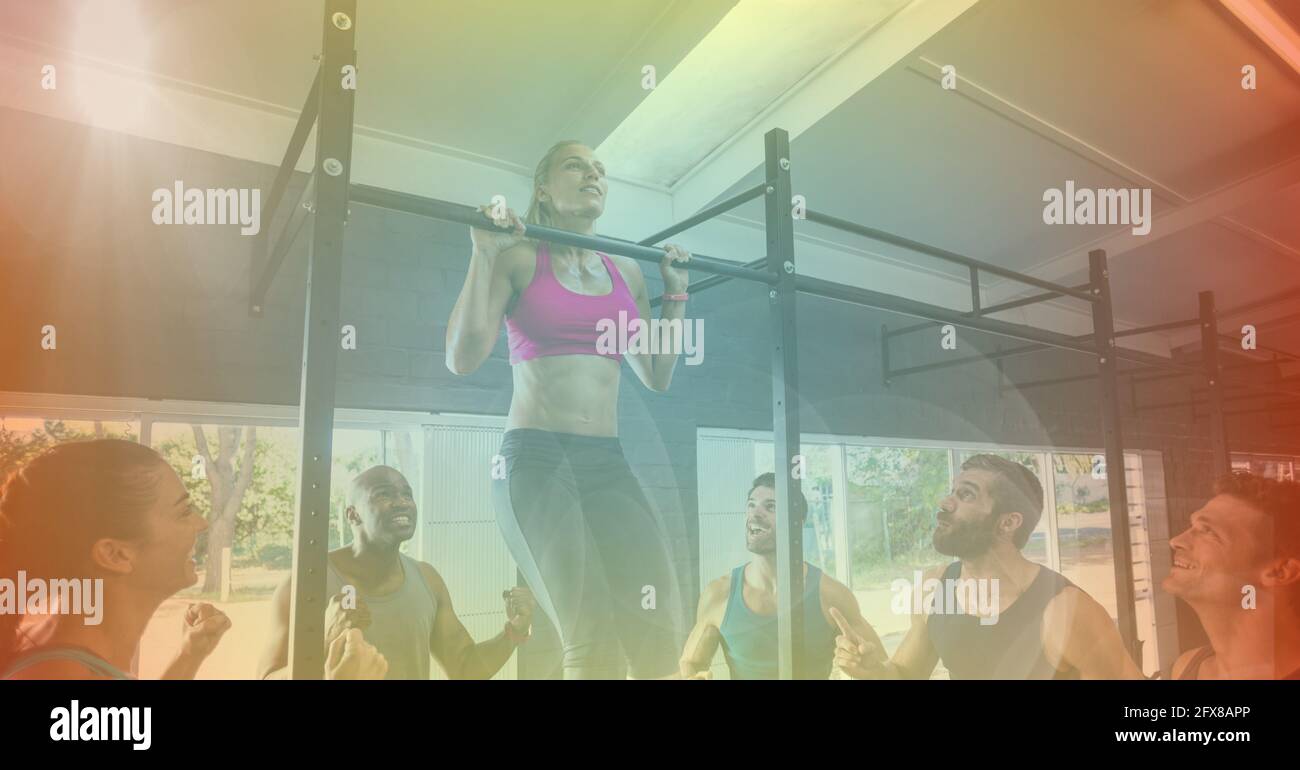Strong woman pulling up on bar exercising in gym her friends cheering ...
