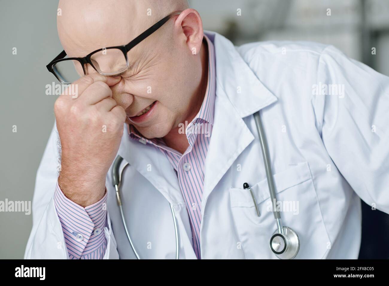 Exhausted mature Caucasian doctor with stethoscope around neck rubbing