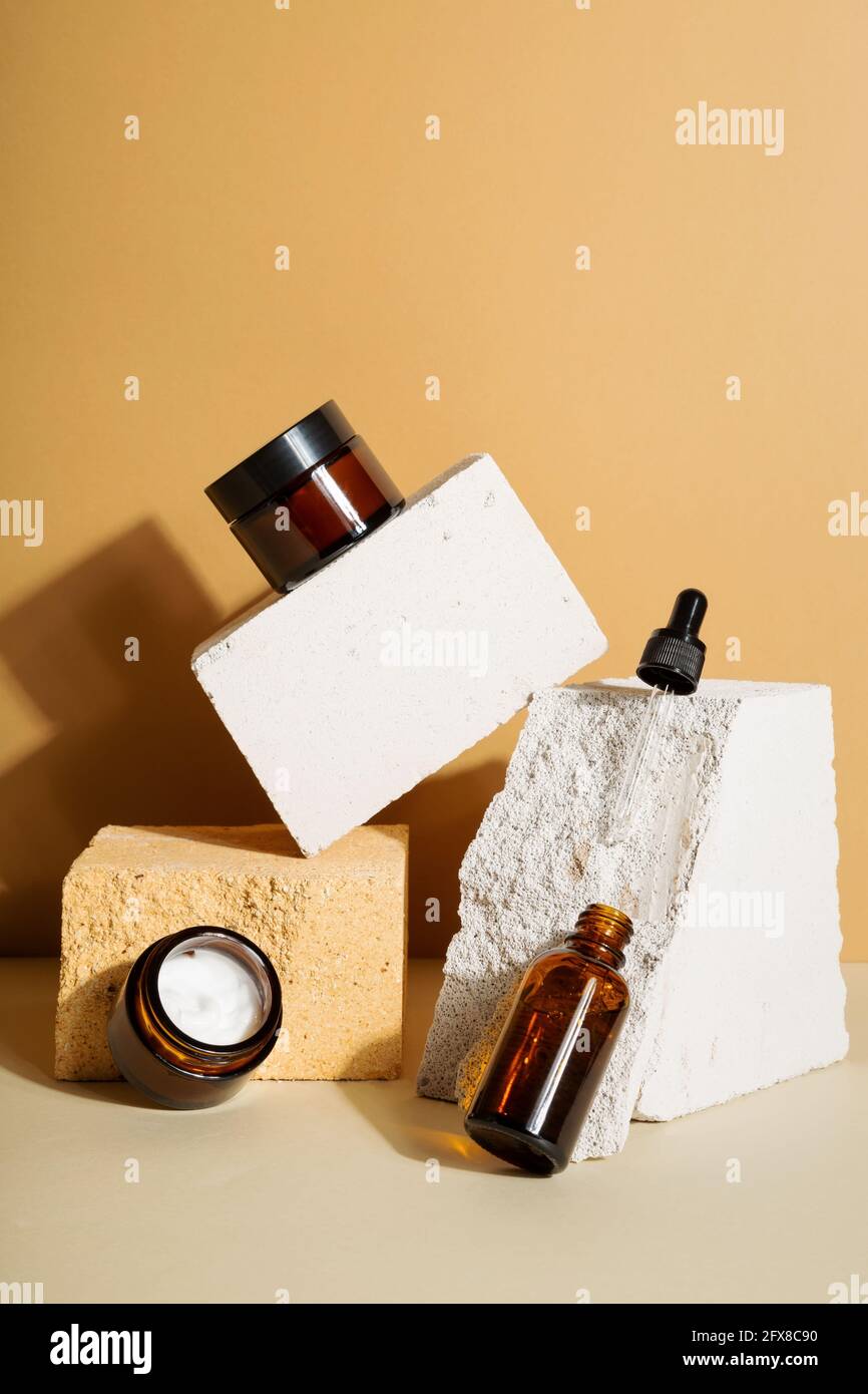 Moisturizers creams jars, serum in glass bottle and white box on beige