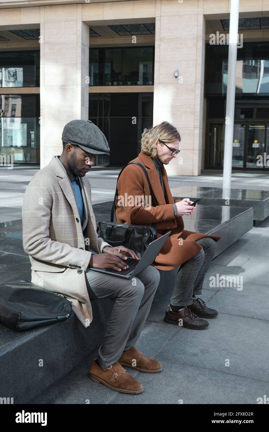 Young people using gadgets and working online while sitting outdoors Stock Photo