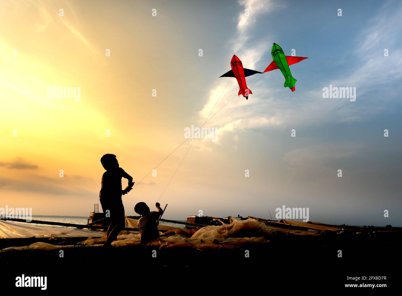 Fishing village children play kite flying at sunset, silhouette