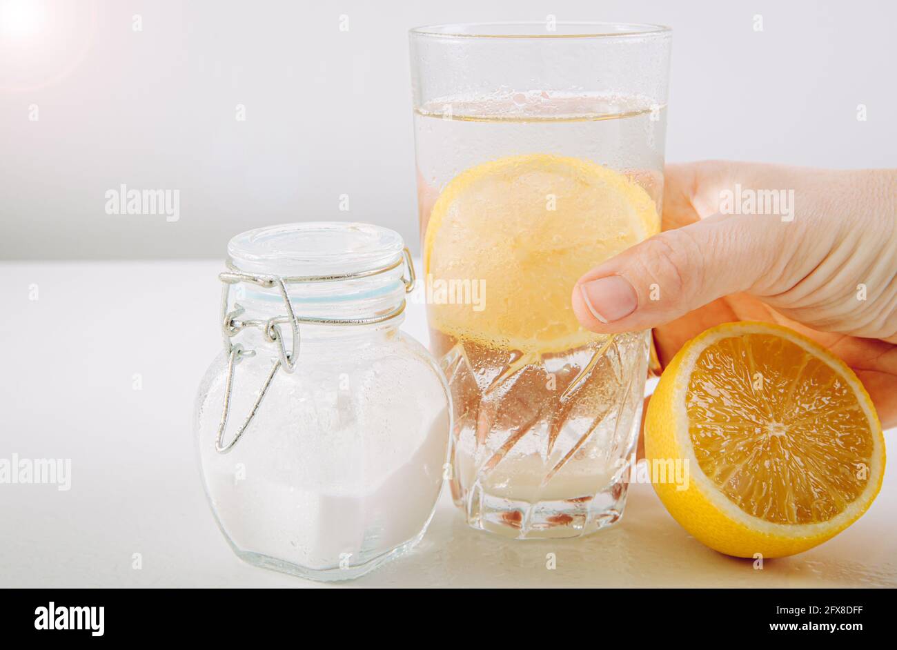 Hand holding drinking glass with baking soda, water and lemon juice infusion, health benefits for digestive system concept. Minimal white background. Stock Photo
