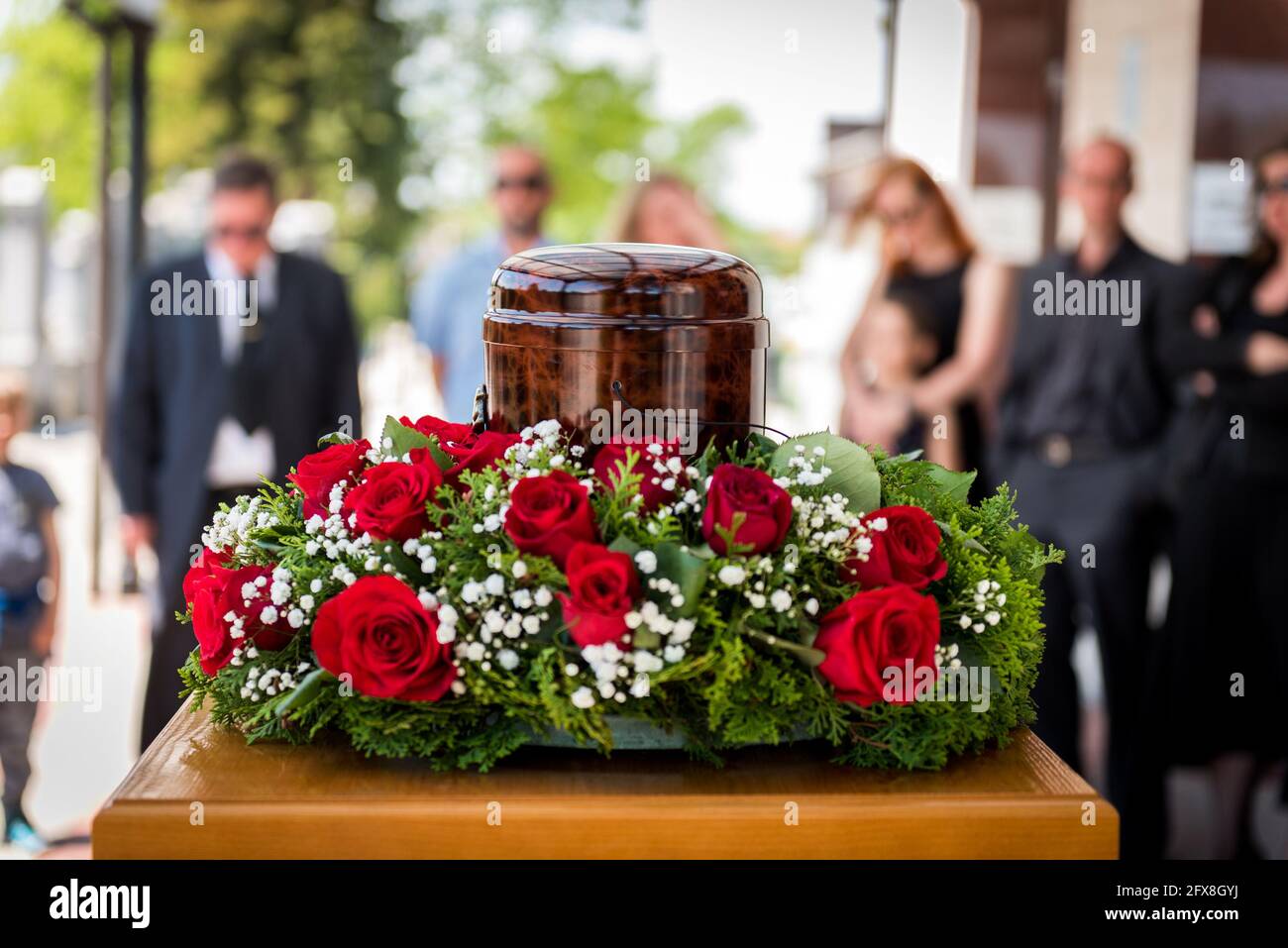 Funerary urn with ashes of dead and flowers at funeral. Burial urn decorated with flowers and people mourning in background at memorial service, sad a Stock Photo