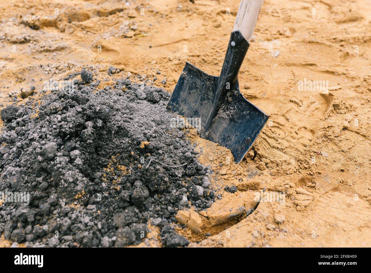 Black shovel in the sand. A tool for scooping up sand in construction work. Sand for construction and planting works. Stock Photo