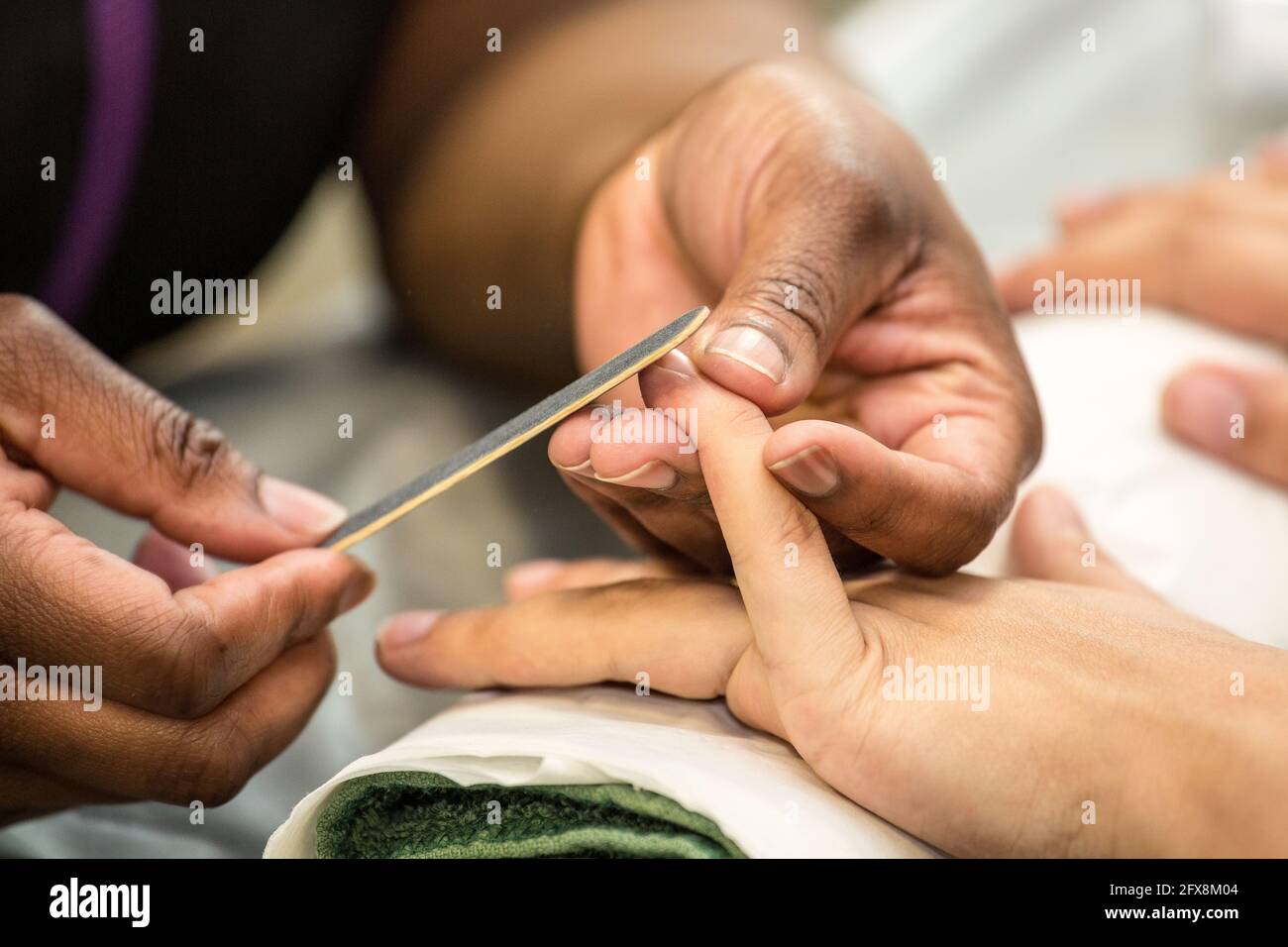 A Caucasian female having her fingernails being manicured by ab Afro-Caribbean female in a beauty parlour, her other hand resting on a towel Stock Photo