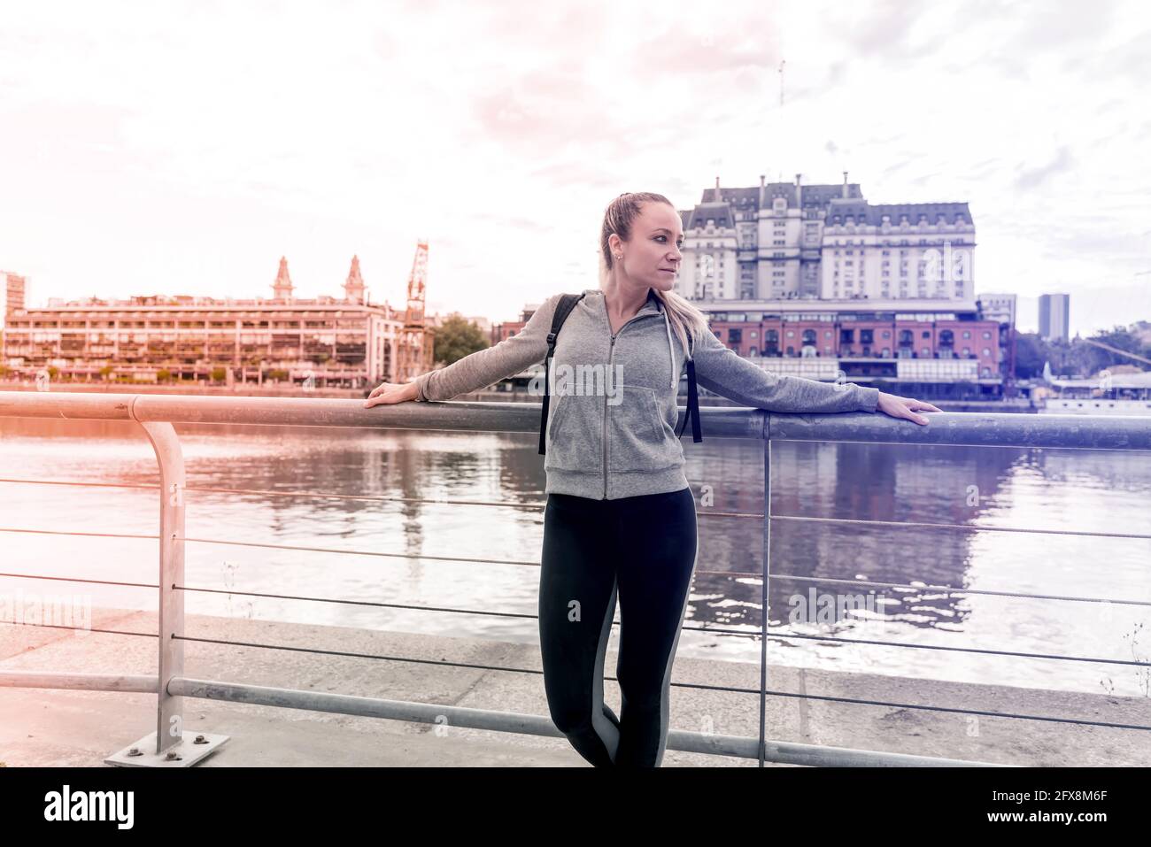 An athletic woman in a grey sweater standing next to the bridge railing. Stock Photo
