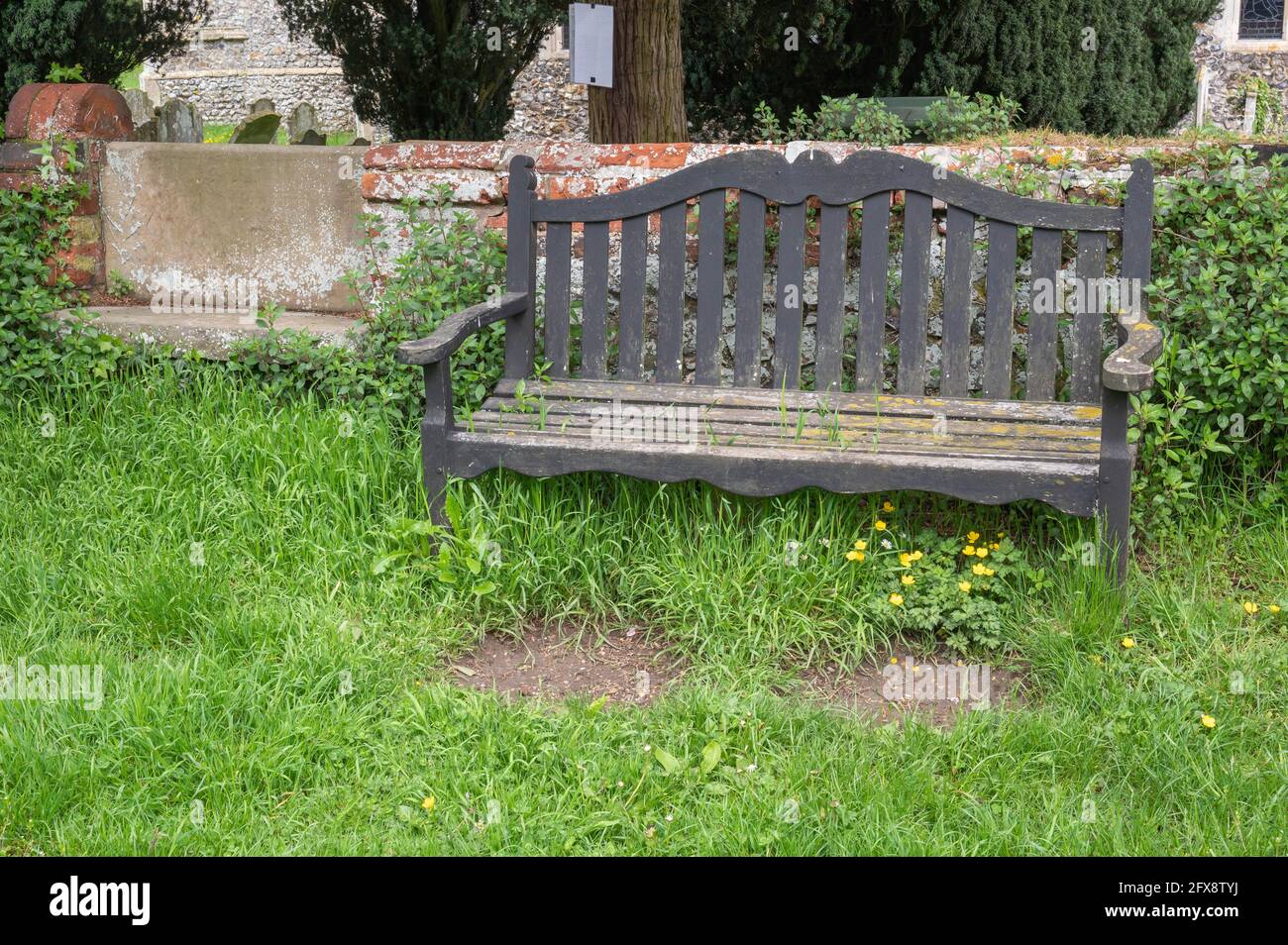 An old distressed wooden park bench set in a church yard in mid Norfolk England Stock Photo
