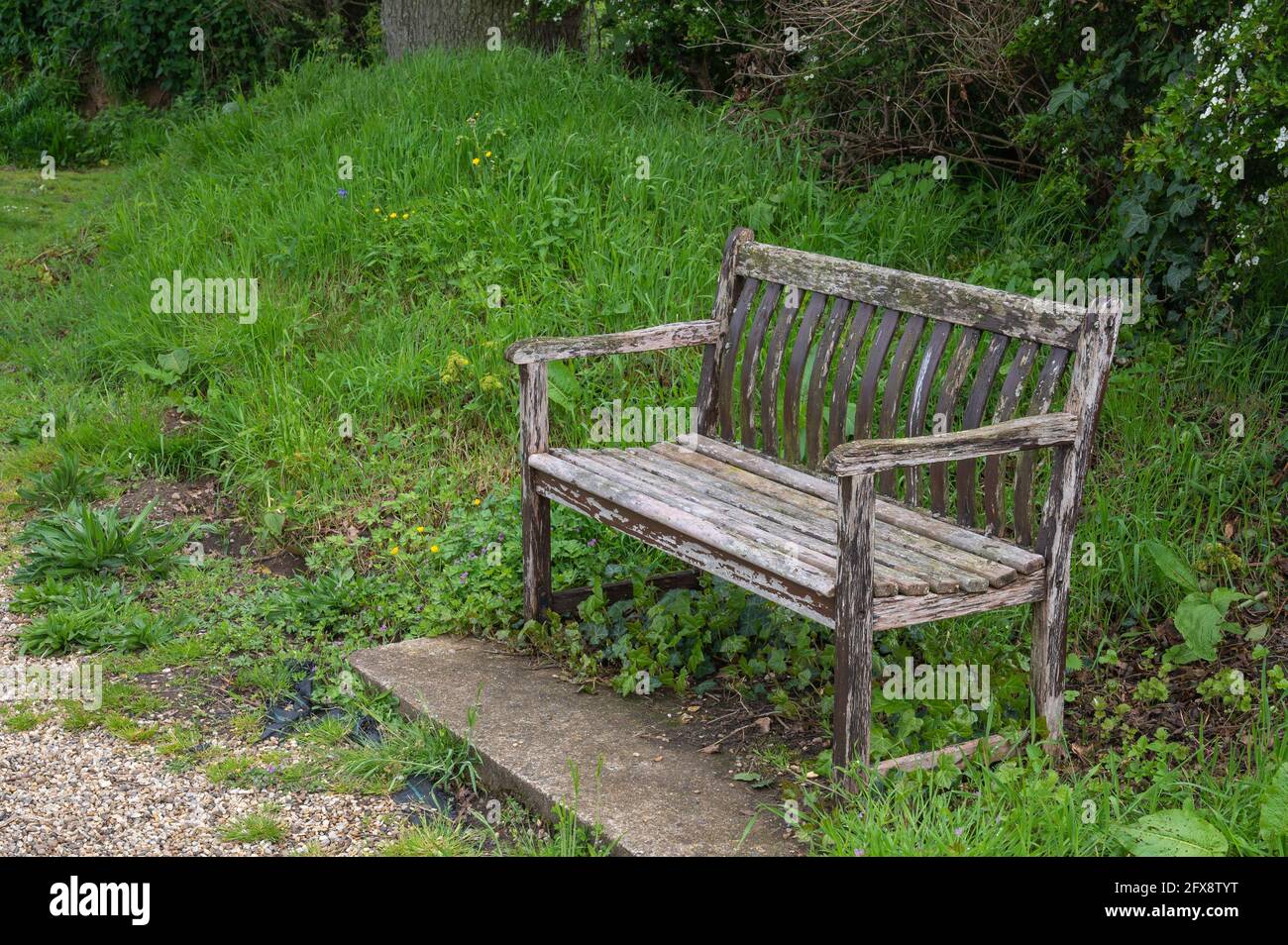 An old distressed wooden park bench set in a church yard in mid Norfolk England Stock Photo