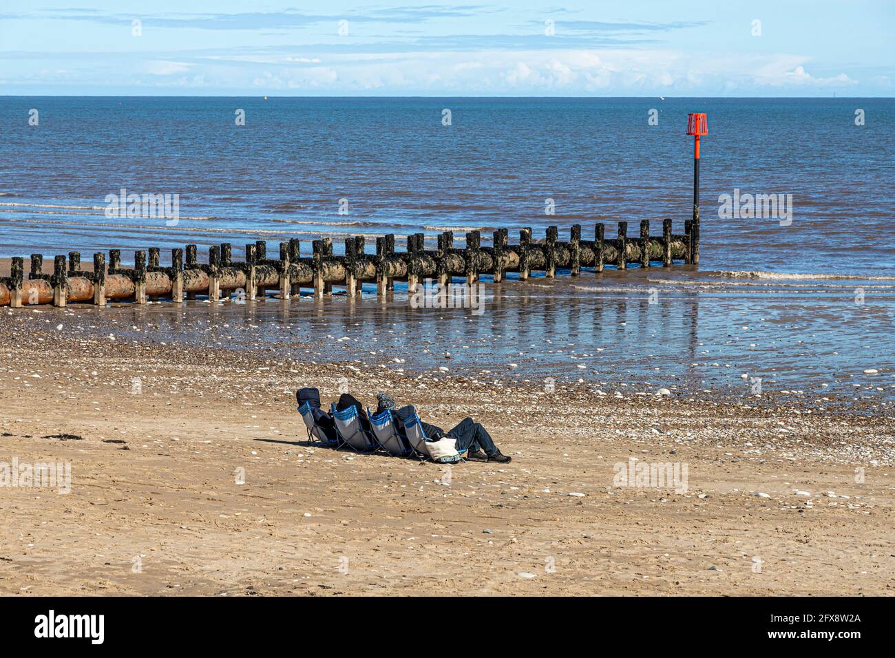 Four people sunbathing in the middle of April beside the North Sea at Bridlington, East Riding of Yorkshire, England UK. Black & white version 2FX8TYW Stock Photo