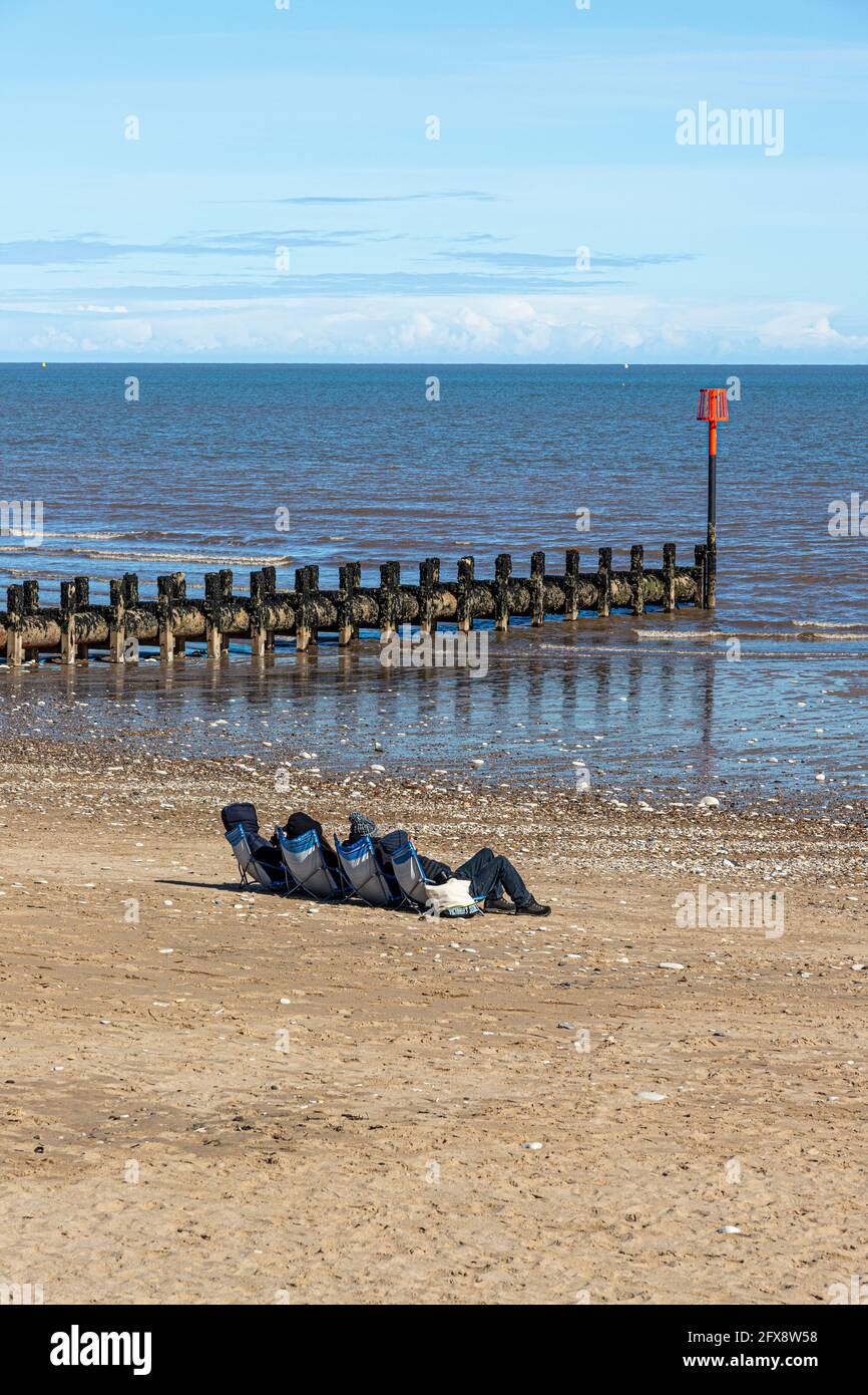 Four people sunbathing in the middle of April beside the North Sea at Bridlington, East Riding of Yorkshire, England UK.. Black & white version 2FX8W4 Stock Photo
