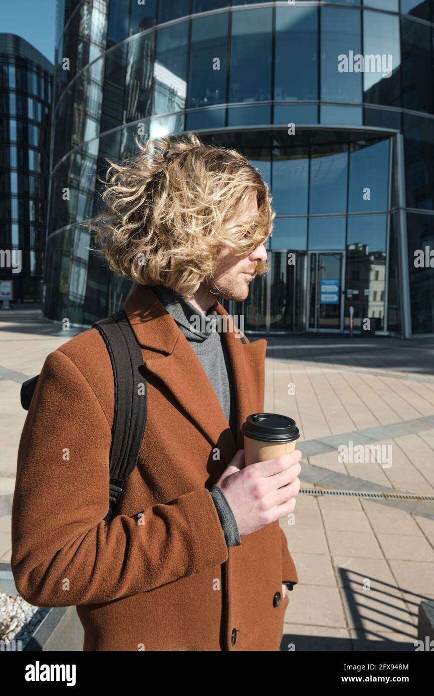 Young man holding disposable cup with coffee while walking outdoors Stock Photo