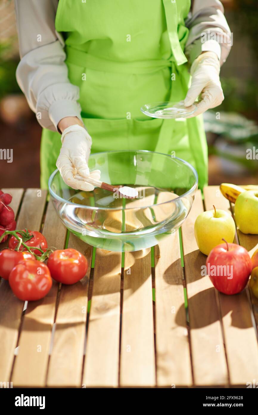 Closeup on housewife in green apron removes pesticides by soaking