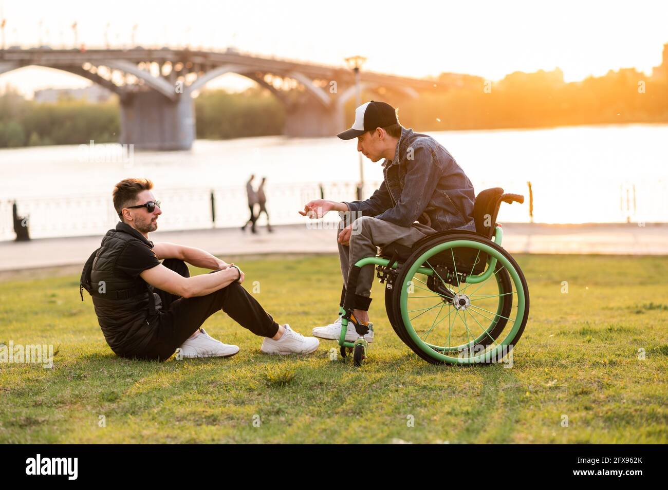 a man in a wheelchair walks with his friend. Man walking with disabled ...