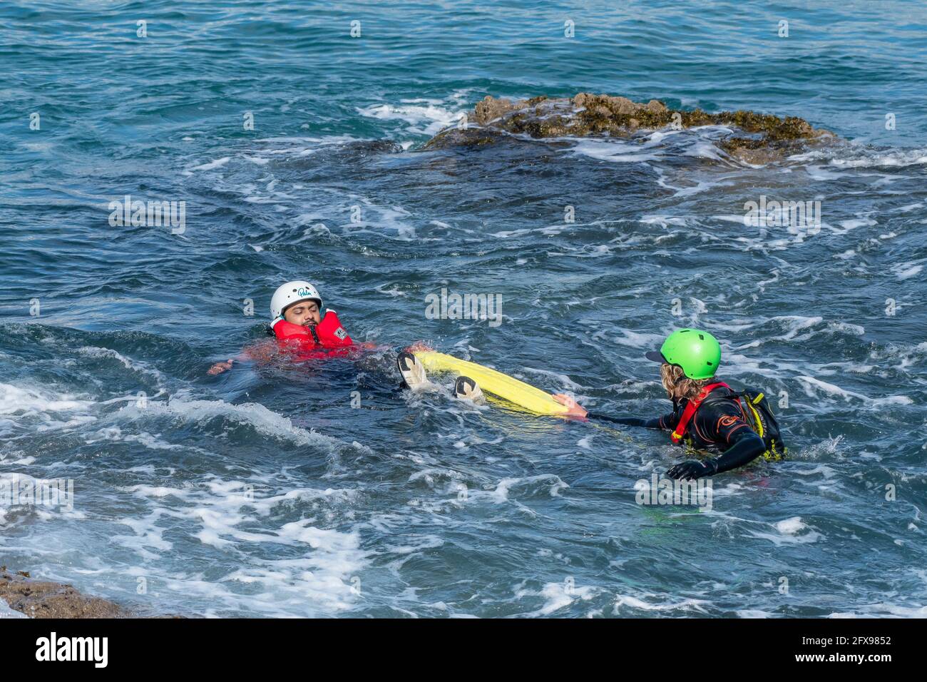 A coasteering guide using a flotation aid to assist a holidaymaker floating in the sea on the coast of Towan Head in Newquay in Cornwall. Stock Photo