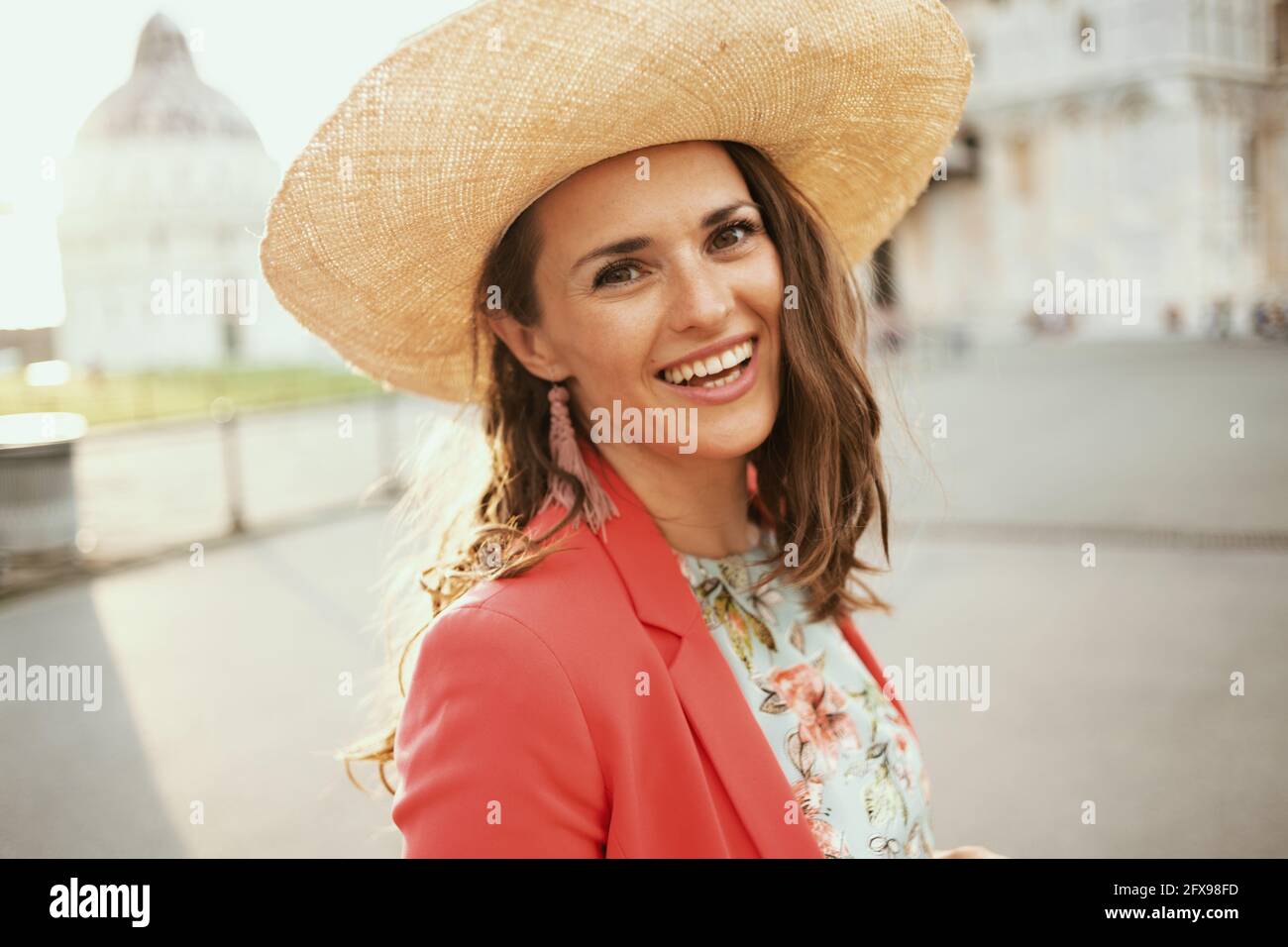 smiling modern middle aged traveller woman in floral dress with hat enjoying promenade in piazza dei miracoli in Pisa, Italy. Stock Photo