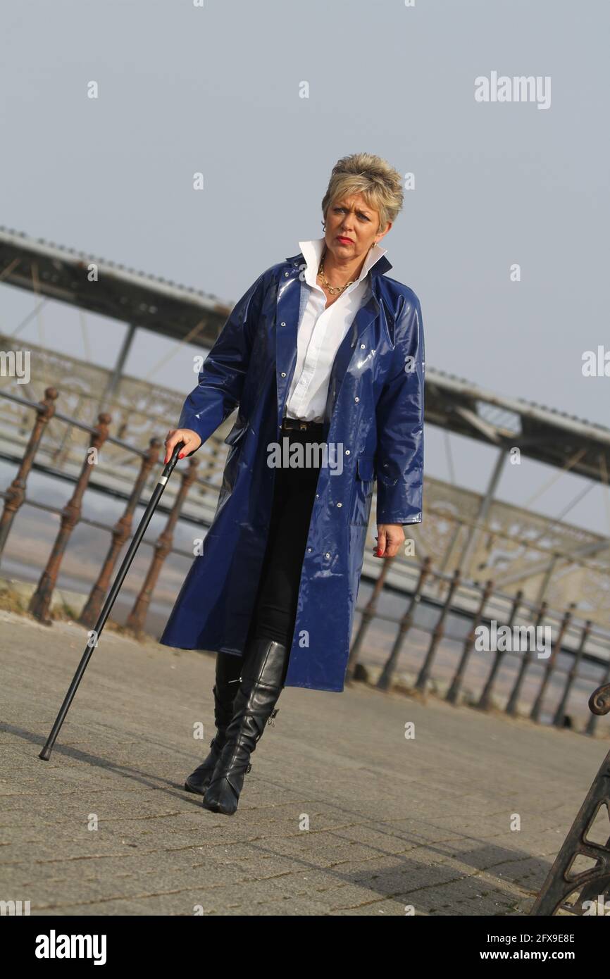 White caucasian middle aged woman with cropped spikey dyed hair wearing blue PVC raincoat Stock Photo