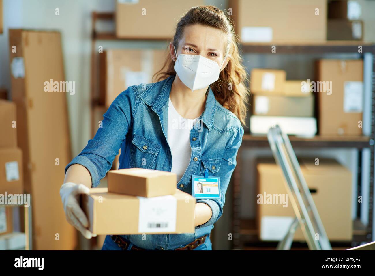 Delivery business. modern female in jeans with ffp2 mask giving parcel in the office. Stock Photo