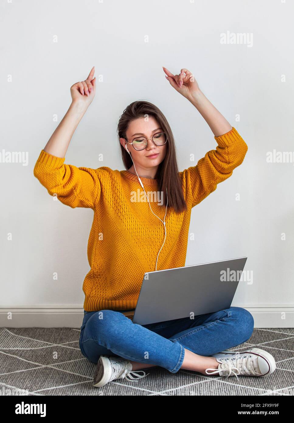 Young woman listening music headphones and dancing, using laptop sitting on carpet on white background Stock Photo
