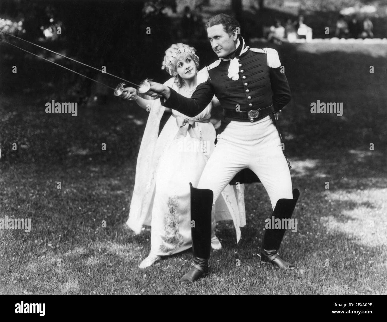 TIM McCOY demonstrating his skills with a sabre to LOUISE LORRAINE on set candid during filming of THE FRONTIERSMAN 1927 director REGINALD BARKER cinematographer Clyde De Vinna costume design Andre-ani Metro Goldwyn Mayer Stock Photo