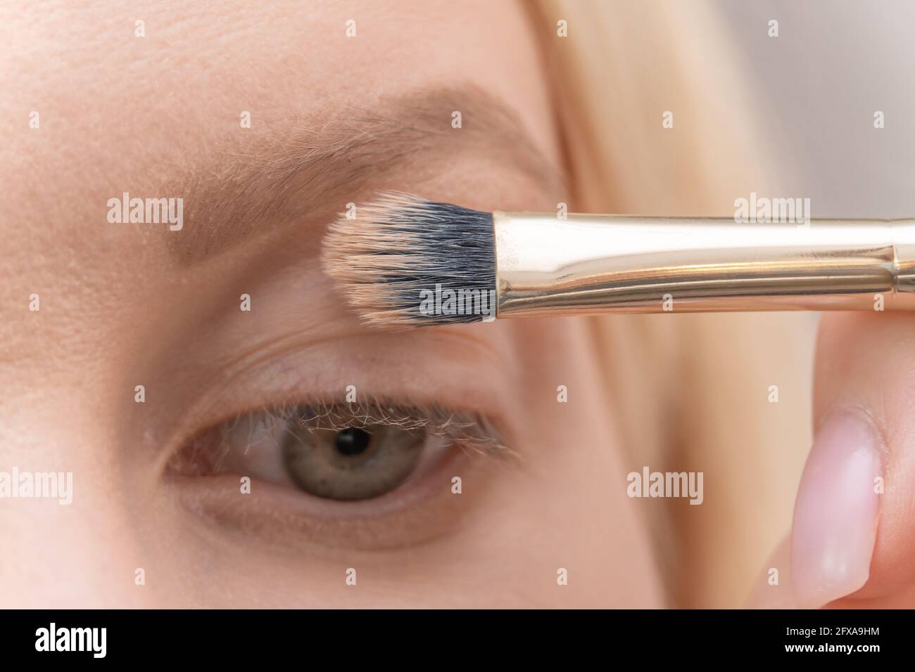 Transfigured Face Close-up brush with concealer over the eye of a blonde girl ...
