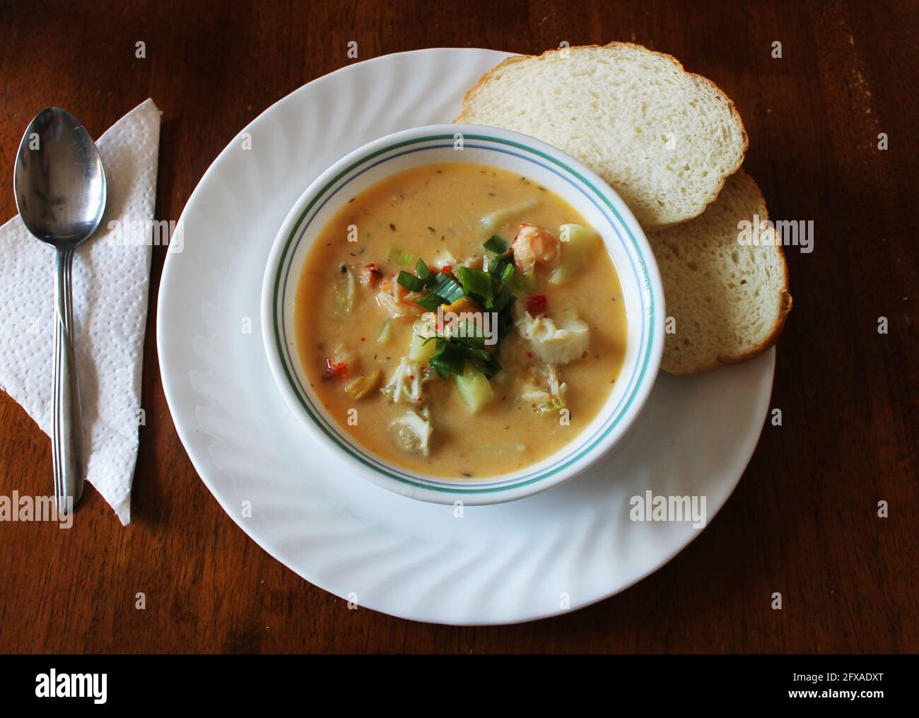 A bowl of homemade seafood chowder with homemade bread. White bowl on a white plate, serviette and spoon. Stock Photo