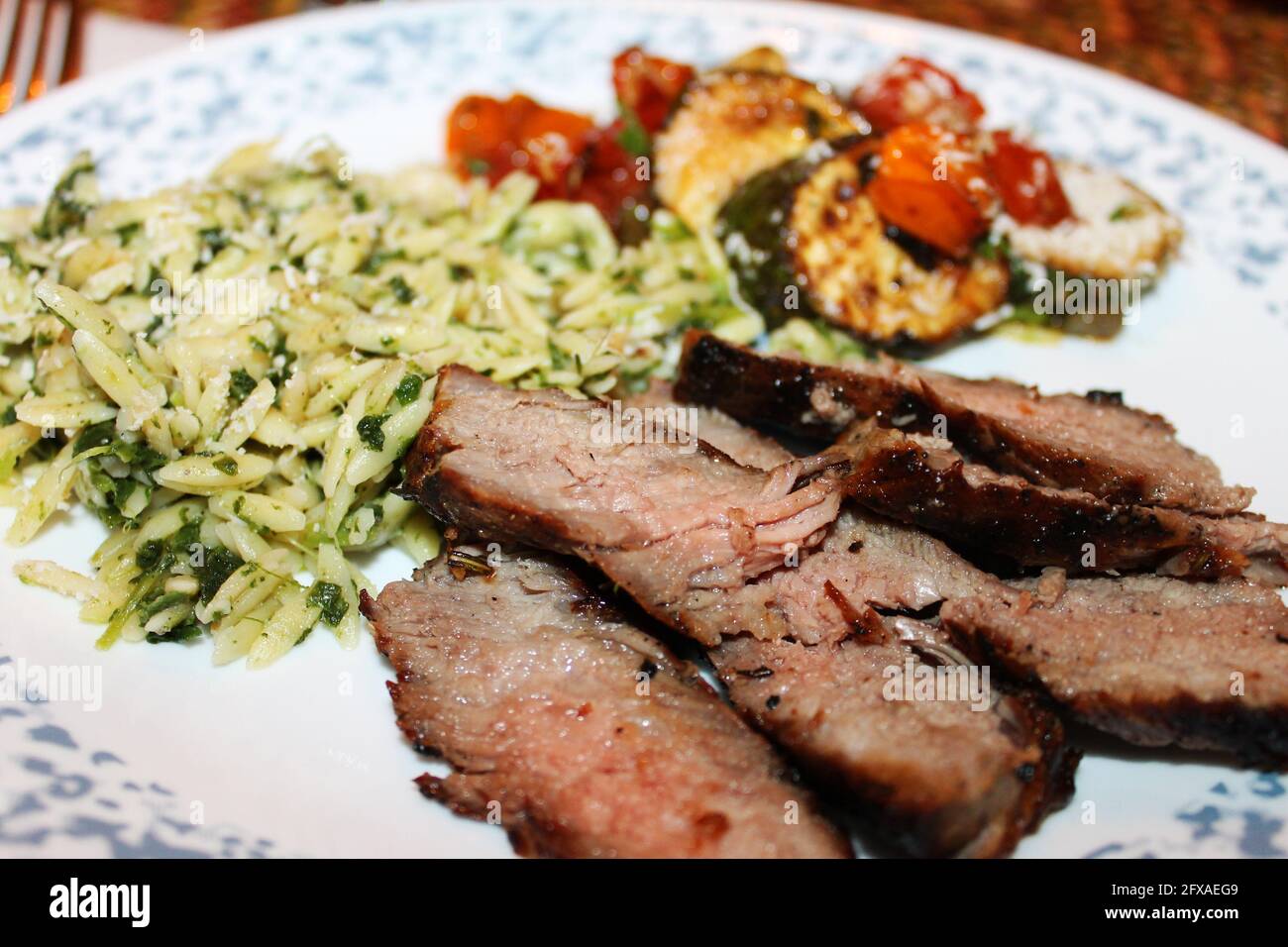 Close-up of a serving of Tuscan Steak with orzo, fried zucchini and cherry tomatoes. Stock Photo