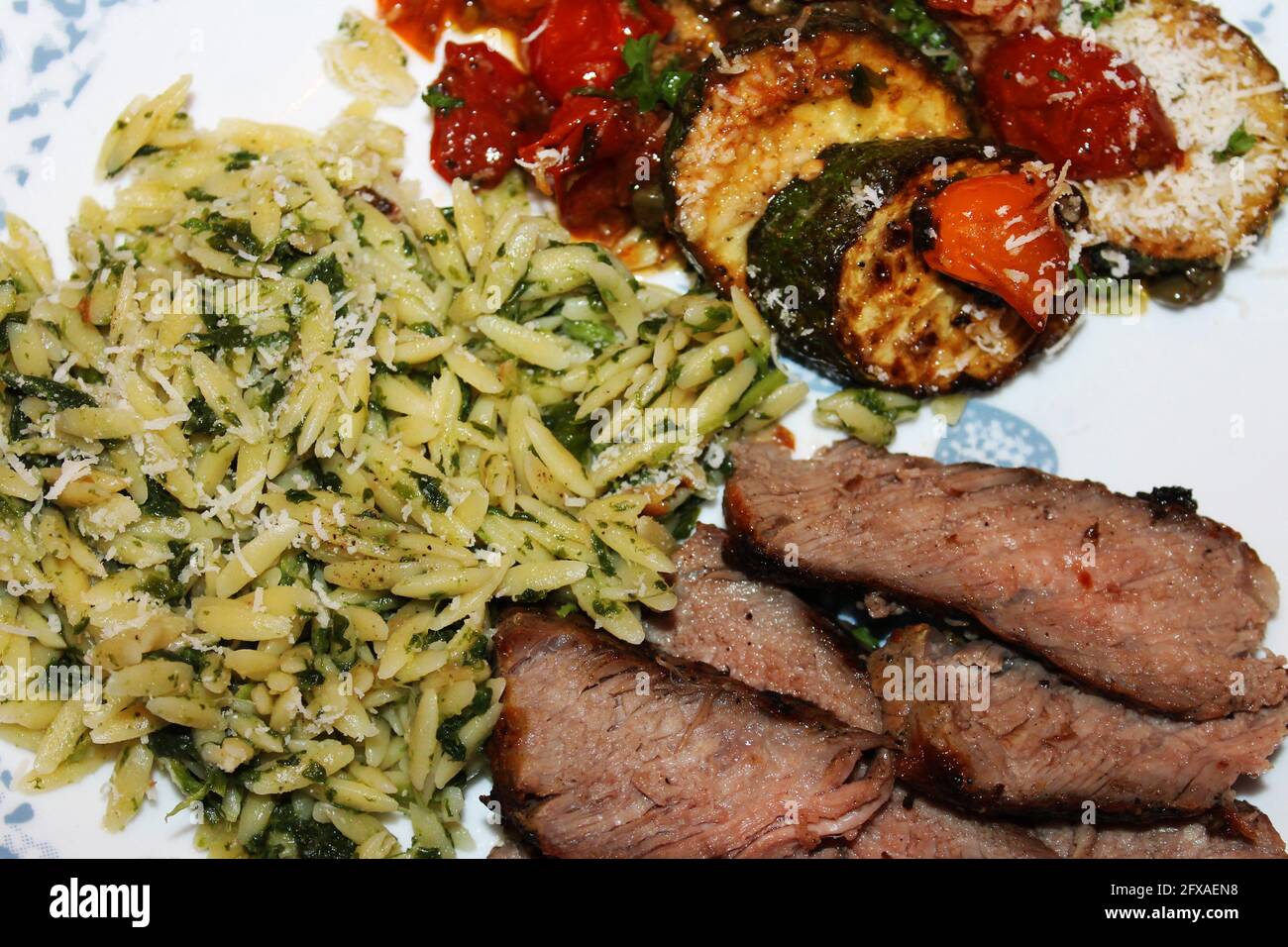Close-up of a serving of Tuscan Steak with orzo, fried zucchini and cherry tomatoes. Stock Photo