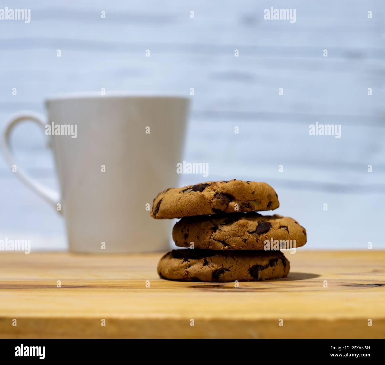 Pile of three Chocolate chips cookies with a coffee cup on a wooden table, white empty background Stock Photo