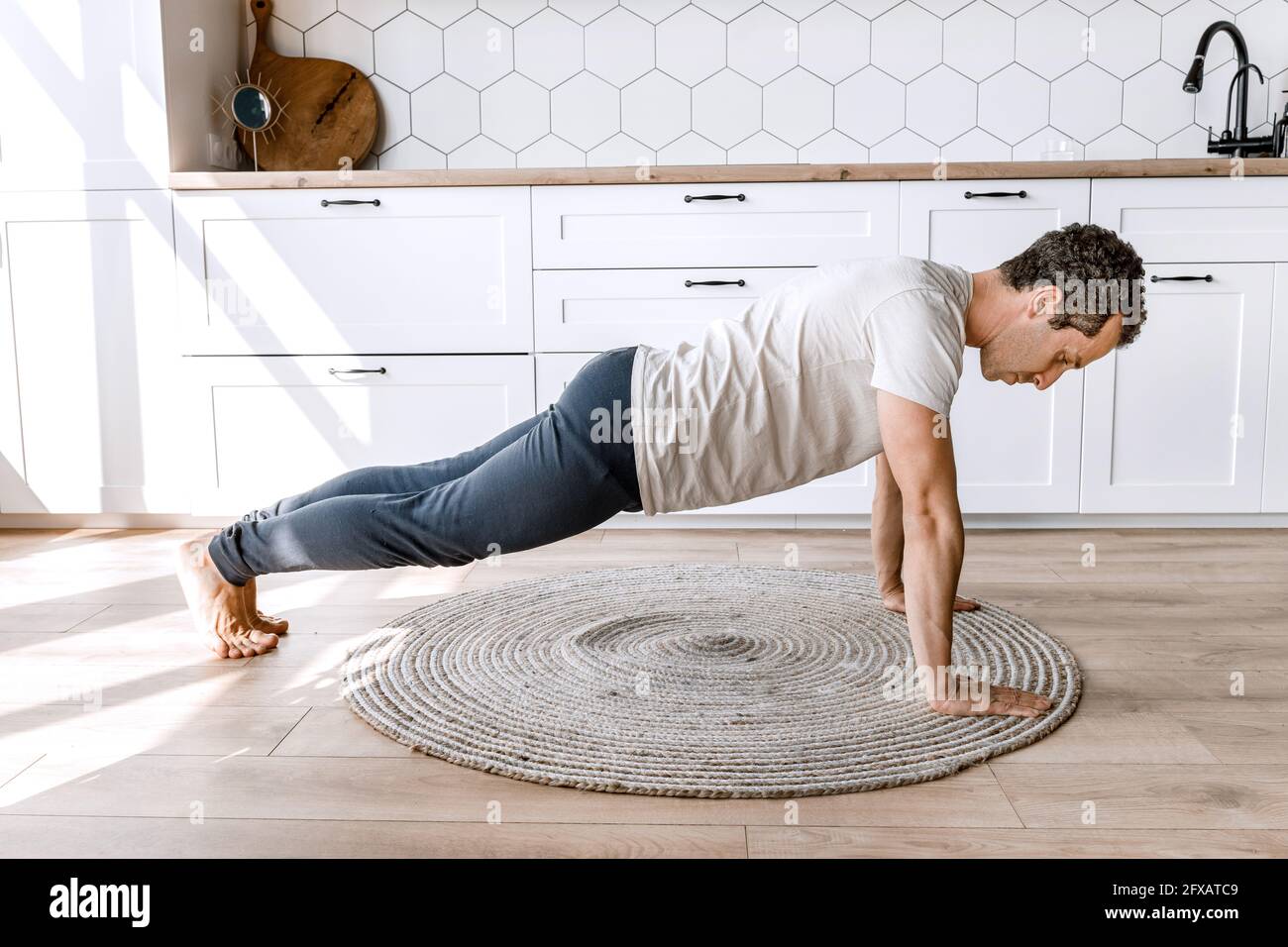 Young athletic attractive man practicing yoga lesson at home on the floor, doing push-ups exercises, standing in plank pose to keep fit Stock Photo