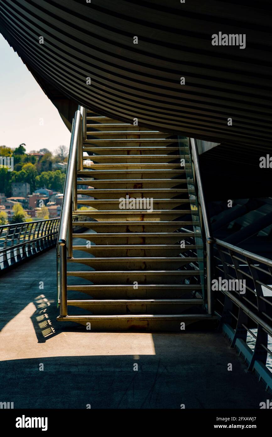 A sunlit stairway to  upper deck of a bridge with some cityscape in the background. Stock Photo