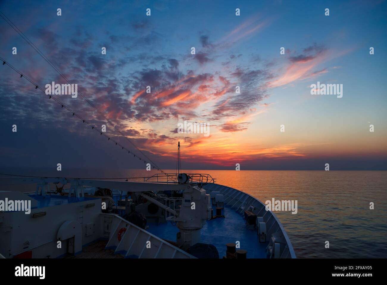 Bow of a passenger cruise ship moving in the open sea towards a stunning pink and orange sunset sky. View from the top. Stock Photo