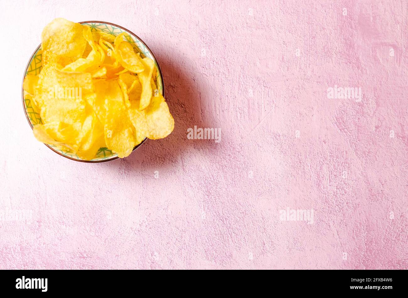 Bowl of potato chips on pink textured background. Image with copy space Stock Photo