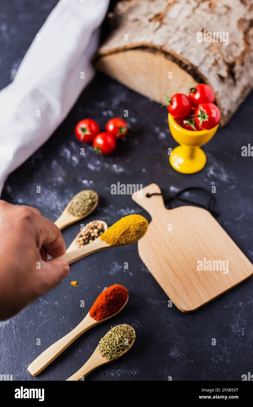 Hand holding a wooden spoon with spices and cherry tomatoes on the table Stock Photo