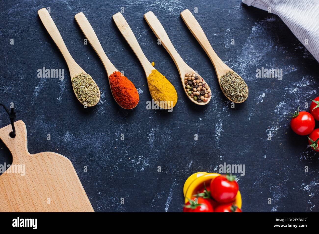Wooden spoons with spices, paprika, basilic, pepper, thyme with cherry tomatoes Stock Photo