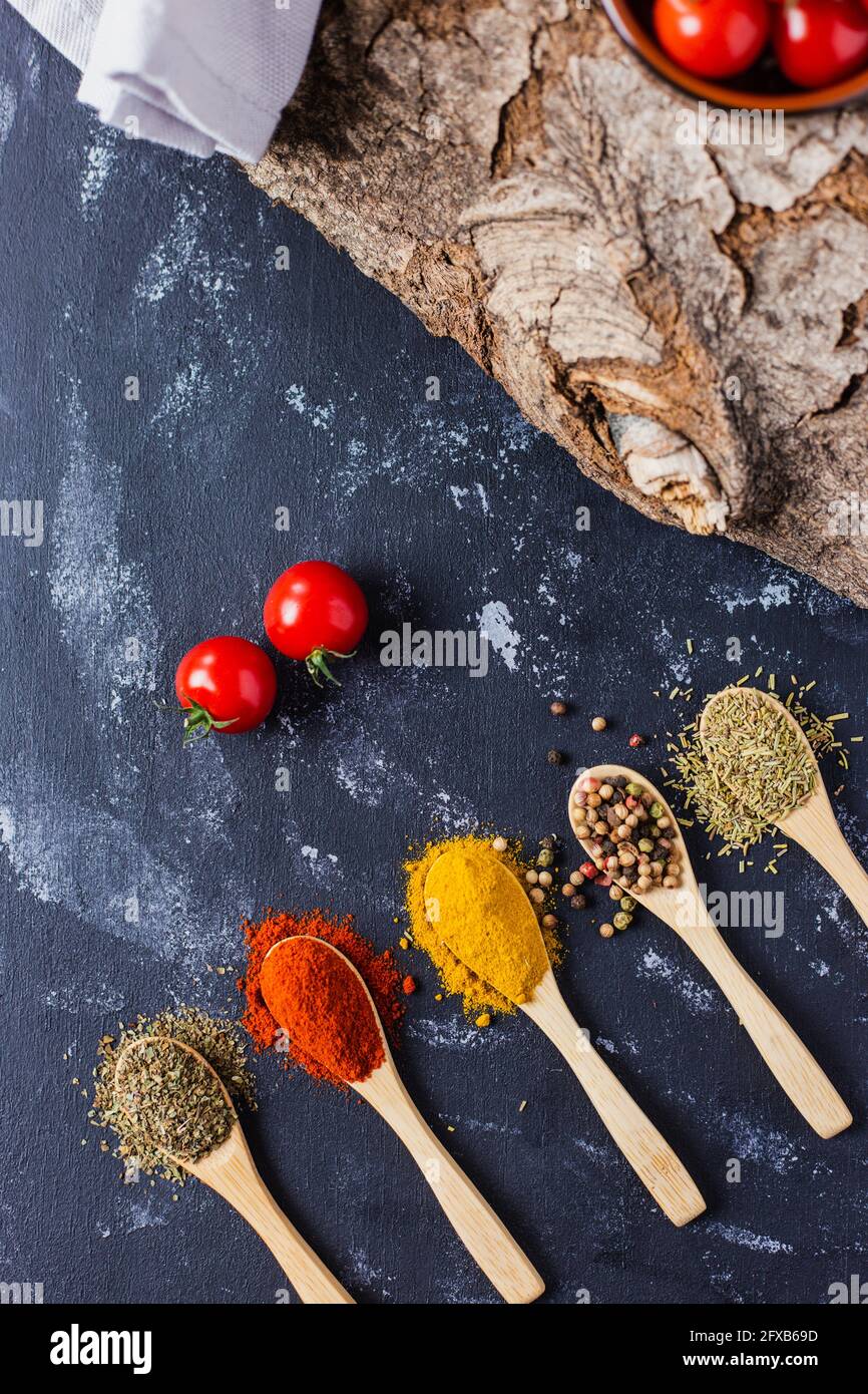 Wooden spoons with spices, paprika, basilic, pepper, thyme with cherry tomatoes Stock Photo