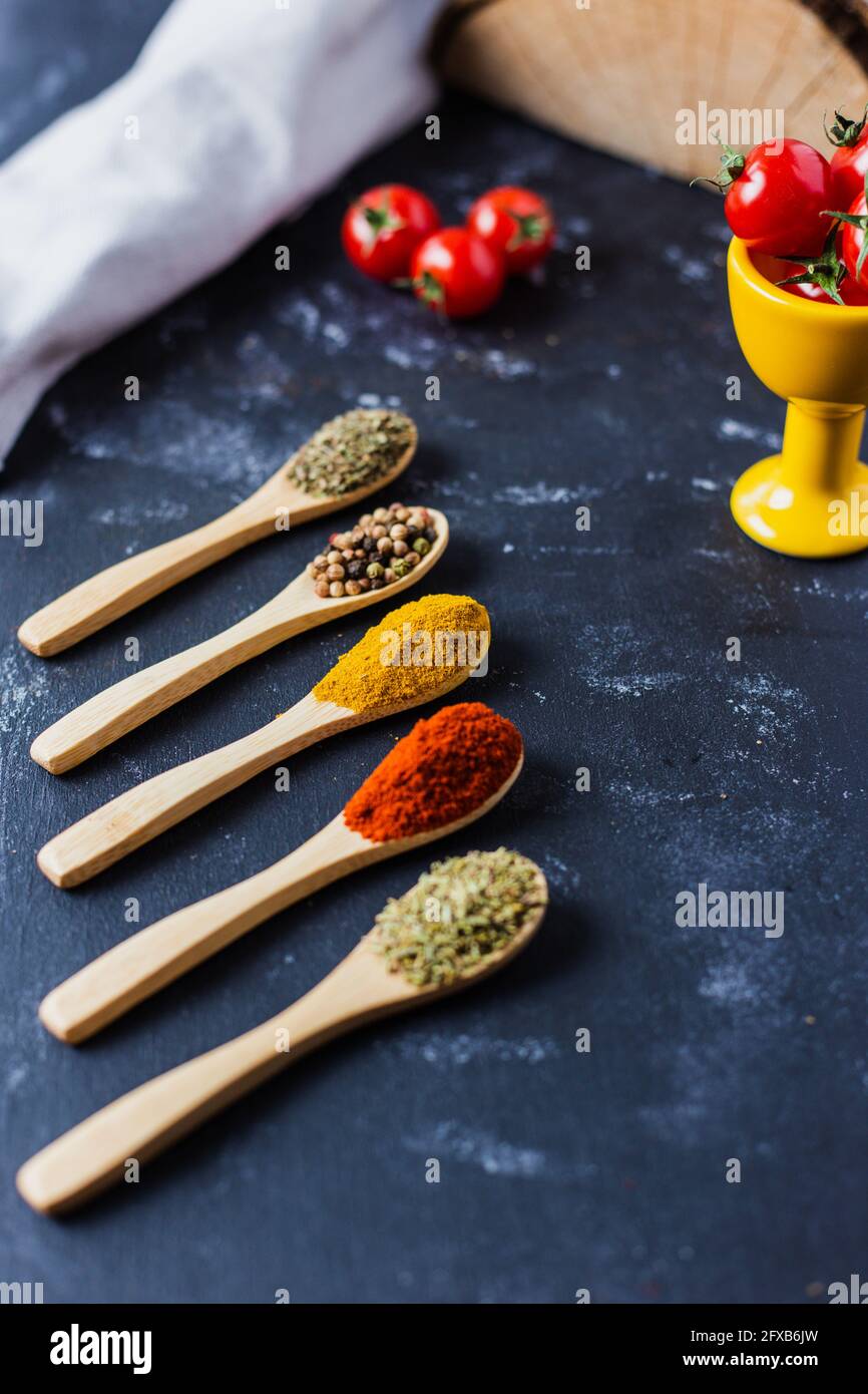 Wooden spoons with spices, paprika, basilic, pepper, thyme with cherry tomatoes Stock Photo