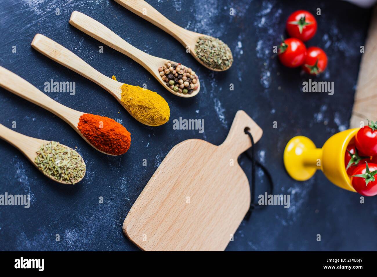 Wooden spoons with spices, paprika, basilic, pepper, thyme with cherry tomatoes Stock Photo