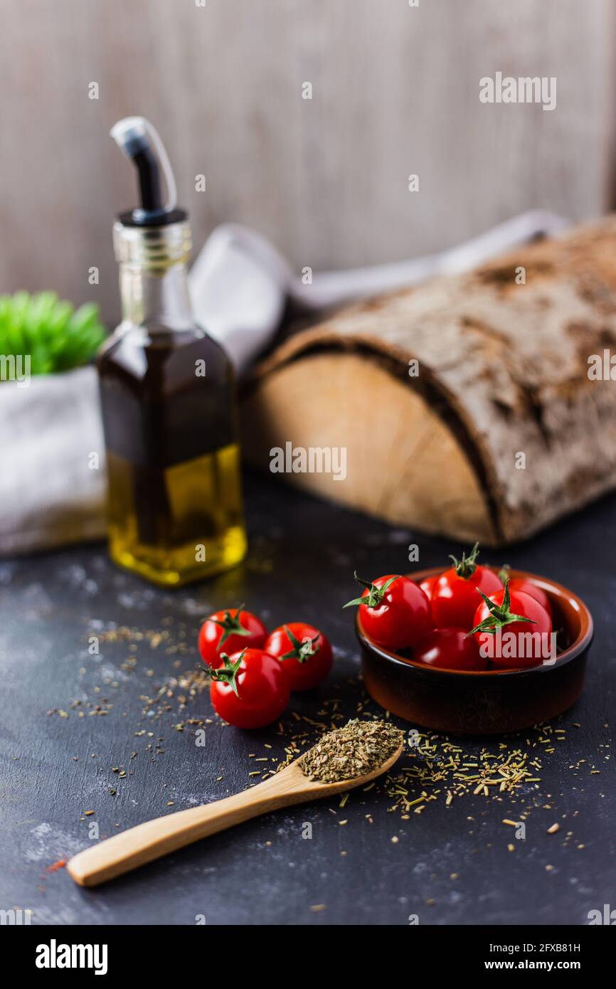 Spoon with spices, cherry tomatoes and a bottle of olive oil on a dark table Stock Photo