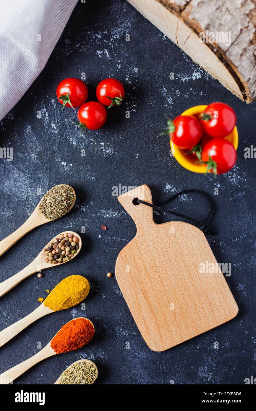 Wooden spoons with spices, paprika, basilic, pepper, thyme with cherry tomatoes Stock Photo