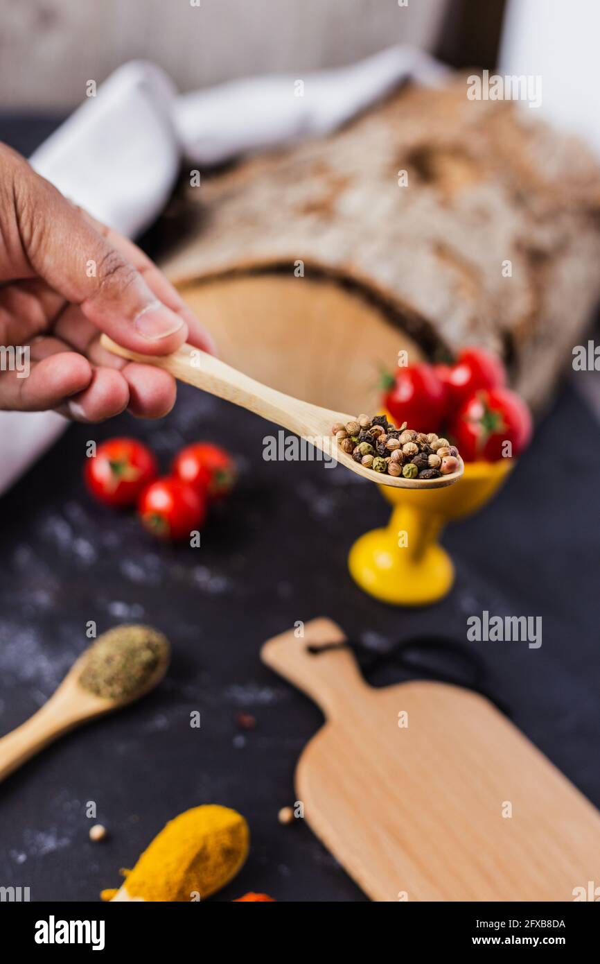 Hand holding a wooden spoon with spices and cherry tomatoes on the table Stock Photo