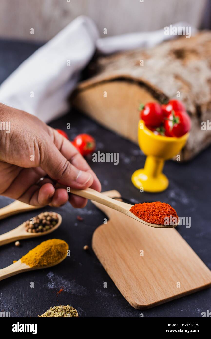 Hand holding a wooden spoon with spices and cherry tomatoes on the table Stock Photo