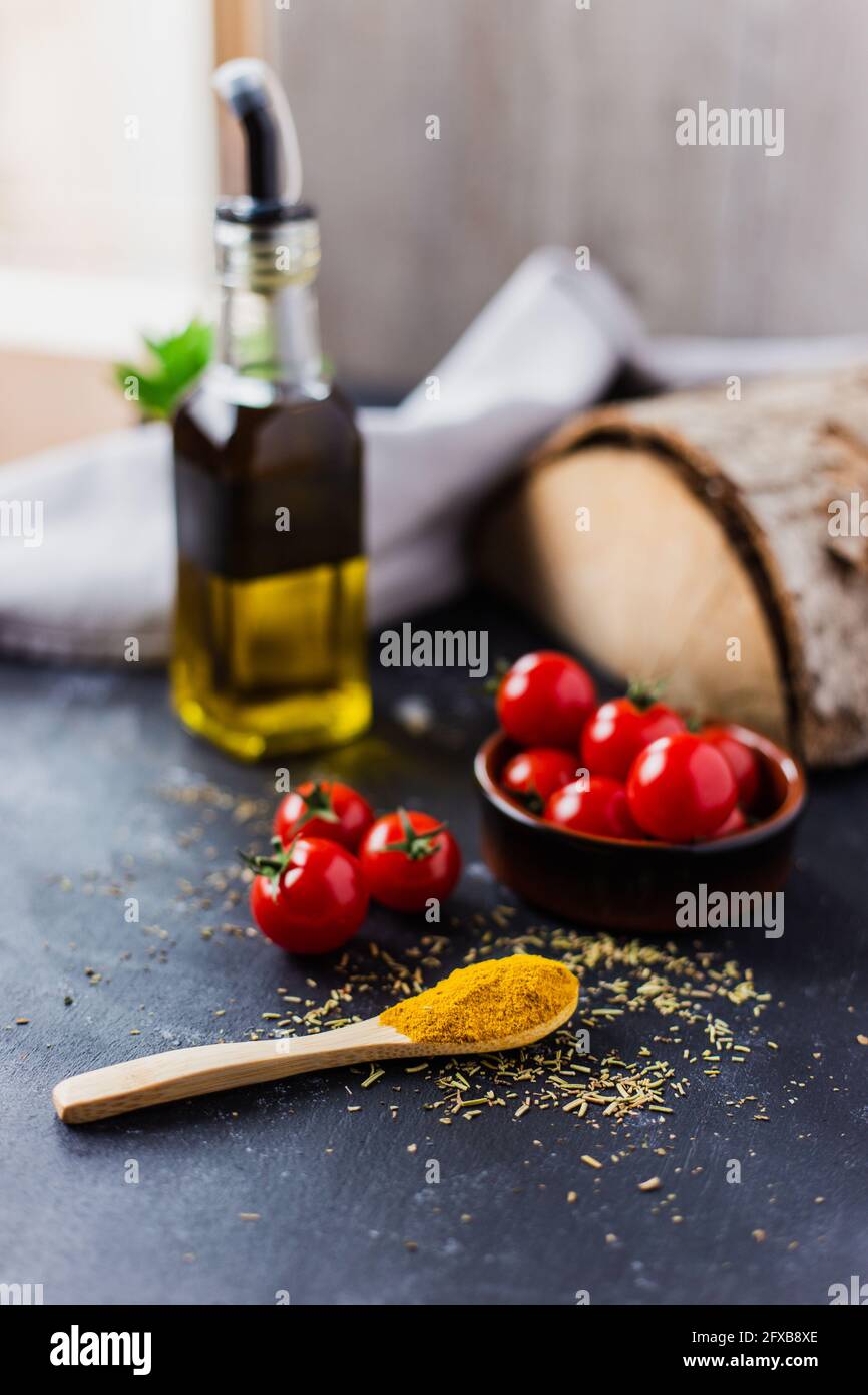Spoon with spices, cherry tomatoes and a bottle of olive oil on a dark table Stock Photo