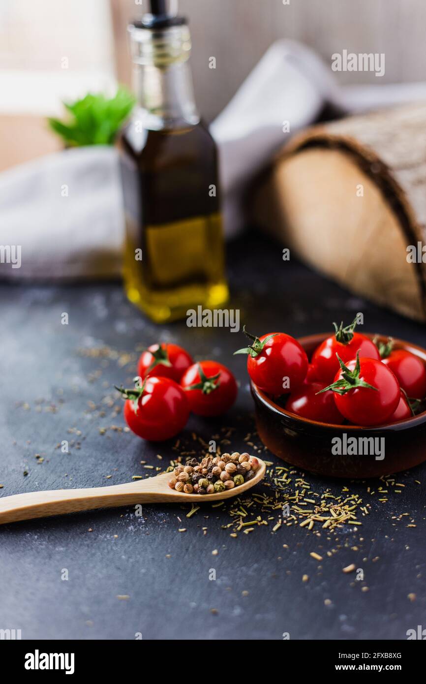 Spoon with spices, cherry tomatoes and a bottle of olive oil on a dark table Stock Photo